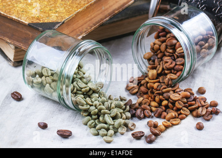 Glass jars with green and brown decaf unroasted coffee beans on table with vintage books Stock Photo