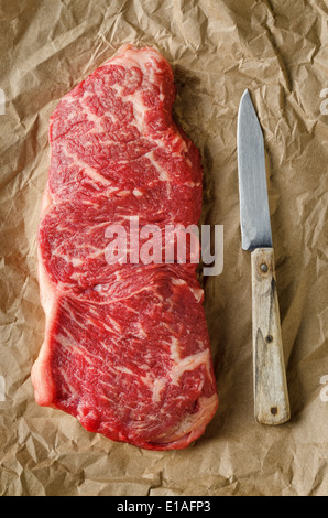 A perfectly marbled strip loin steak on crumpled butcher paper with old knife. Stock Photo