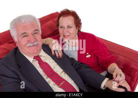 High angle view of an attractive stylish senior couple seated together on a red couch looking up at the camera with friendly Stock Photo