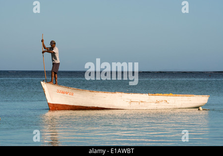 A fisherman poling along in his old wooden boat off the coast of Le Morne Brabant Peninsula on the southwest coast of Mauritius Stock Photo