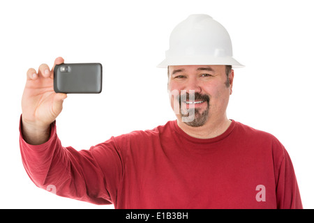 Smiling workman with a goatee beard wearing a hardhat taking a self-portrait using his smartphone, isolated on white Stock Photo