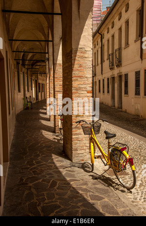 Bicycles standing at the side of a cobbled road leading the eye along a traditional Italian arched walkway in Treviso, Veneto, Stock Photo