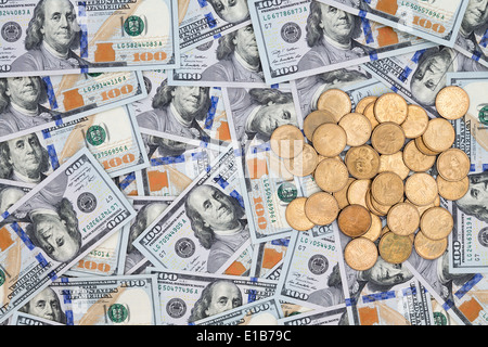 Multiple new randomly scattered American 100 dollar bills with a neat pile of dollar coins viewed from overhead in a conceptual Stock Photo