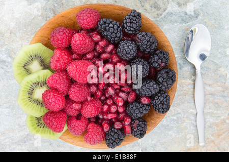 Delicious nutritional snack made of fresh slices of kiwi, seeds of pomegranate, blackberries and raspberries, in a wooden bowl, Stock Photo