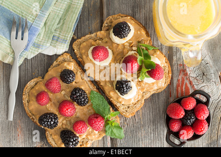 Overhead view of healthy peanut butter sandwiches on wholewheat bread topped with fresh raspberries and blackberries, herbs and Stock Photo