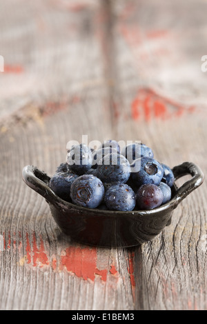 Bowl of fresh ripe autumn blueberries for a healthy diet rich in Vitamin K and antioxidants on old wooden boards in vertical for Stock Photo