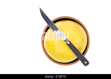 Kitchen knife on a ripe yellow grapefruit or pomelo fitted tightly into a small bowl ready to be cut and prepared for breakfast, Stock Photo
