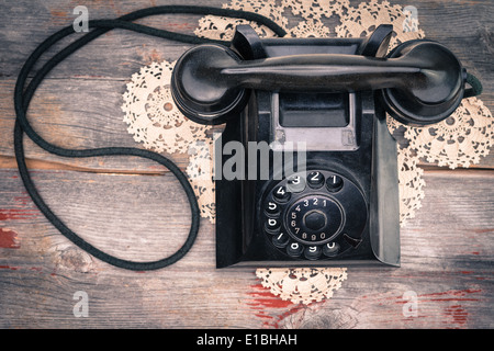 View from above of a black old-fashioned rotary telephone instrument on a crocheted doily on a weathered wooden table top Stock Photo