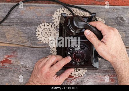 High angle view of the hands of a married man dialing out on an old rotary telephone standing on a weathered rustic table top Stock Photo