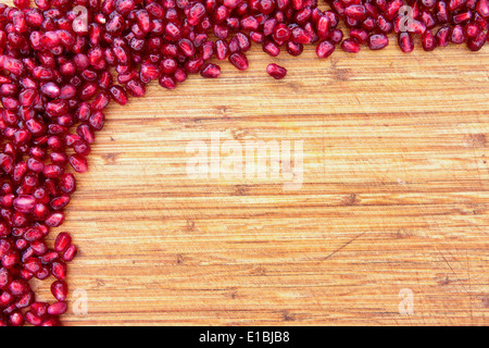 Border of fresh ripe red pomegranate seed on a textured wood background arranged in a pile in the top left corner with ample cop Stock Photo