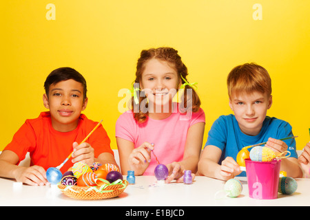 Two boys and girl paint Easter eggs at the table Stock Photo