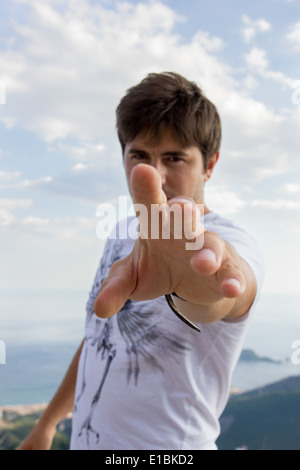handsome man extends his hand to the camera with blue sky and sea behind him Stock Photo