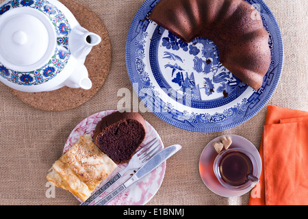 Turkish borek and chocolate cake served for tea with a traditional Turkish teapot and glass of tea on a neutral colored mat Stock Photo