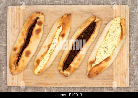 Four traditional baked Turkish pides, an unleavened flat bread topped with savory ground beef meat and cheese and served on wood