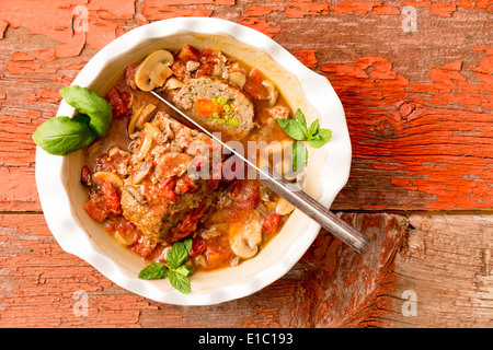 Sliced savory meatloaf with mushrooms and vegetables served in a casserole on a rustic wooden table with grungy peeling red pain Stock Photo