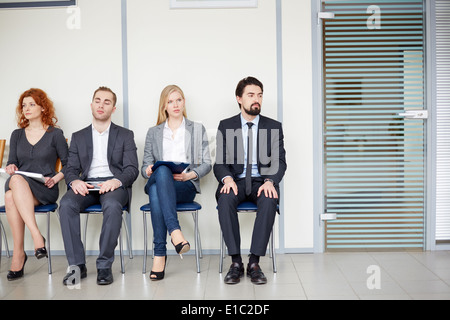 Portrait of several business associates sitting on chairs by office door Stock Photo