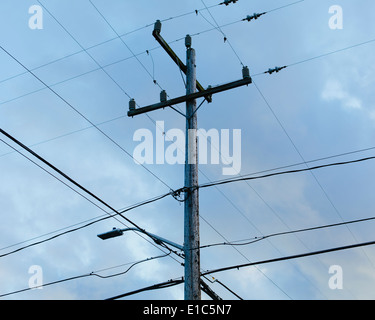 Telephone pole and electrical power lines viewed from the ground, against a cloudy sky. Stock Photo