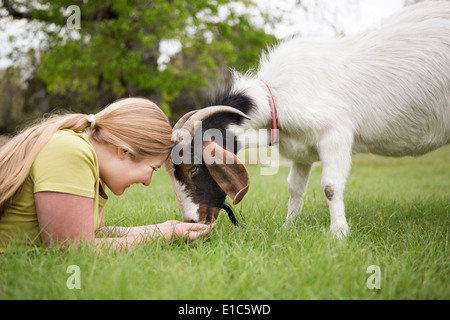 A girl lying on grass head to head with a goat. Stock Photo