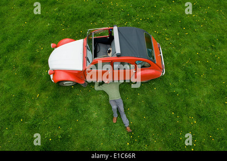 A man lying on his back under a red car, inspecting the underside of the car.