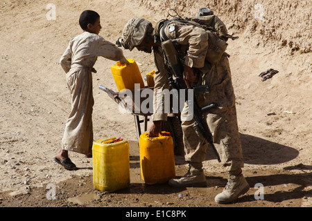 U.S. Marine Corps Lance Cpl. Kevin Choeun helps an Afghan boy reload his wheelbarrow with water jugs during a patrol in the Naw Stock Photo