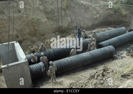 U.S. Soldiers from the 642nd Engineer Support Company and Iraqi construction workers guide a piece of culvert tubing into place Stock Photo