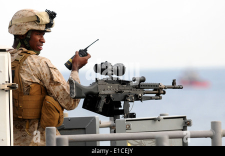 U.S. Marine Corps Lance Cpl. Christian Jones talks on a radio while manning an M-240B machine gun on the starboard side of the Stock Photo