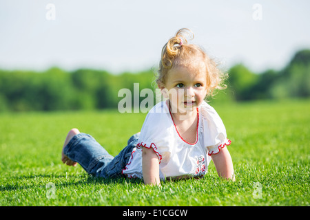 Cute smiling little girl lying on a fresh green grass in a field, Stock Photo