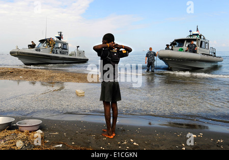A Haitian boy watches as U.S. Sailors in rigid-hull inflatable boats from the amphibious dock landing ships USS Fort McHenry (L Stock Photo