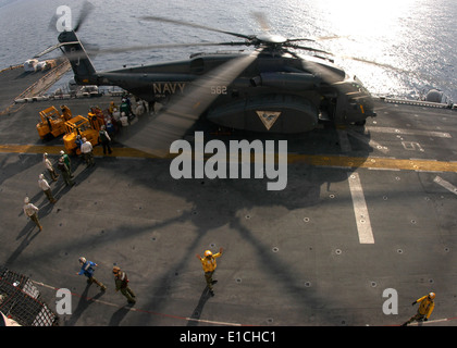 U.S. Navy flight deck personnel unload supplies from an MH-53E Sea Dragon helicopter assigned to Helicopter Mine Countermeasure Stock Photo