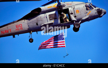 A U.S. Sailor from Explosive Ordnance Disposal Mobile Unit 3 suspends an American flag from an SH-60F Seahawk helicopter during Stock Photo