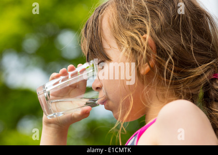 Young caucasian girl drinking from glass with fresh water outdoors during summer time. Stock Photo