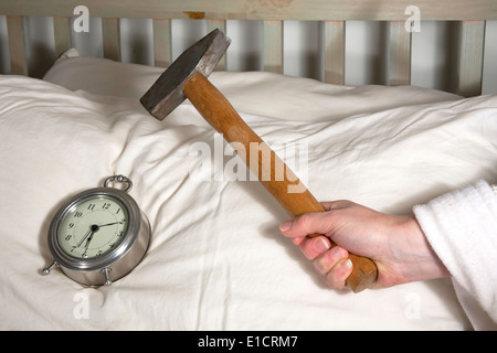 Hand holding a hammer over an alarm clock on a pillow. Stock Photo