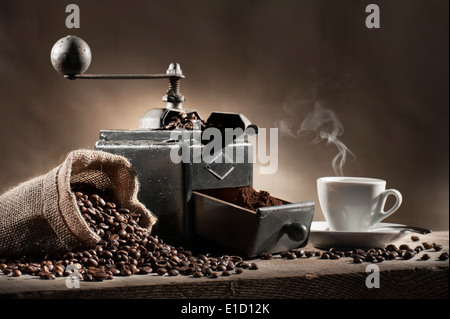 coffee beans in jute bag with coffee grinder and hot cup of coffee on wooden table Stock Photo