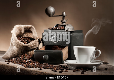 hot cup of coffee with coffee grinder and coffee beans in jute bag on wooden table Stock Photo