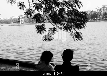 Young Vietnamese couple relaxing by Hoan Kiem lake in Hanoi,Vietnam. Known as the 'Lake Of The Restored Sword'. Stock Photo