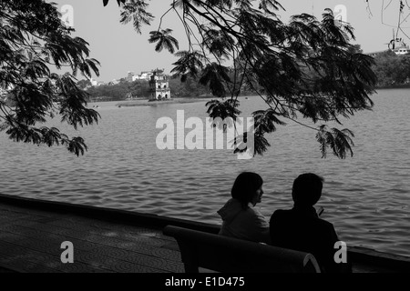 Young Vietnamese couple relaxing by Hoan Kiem lake in Hanoi,Vietnam. Known as the 'Lake Of The Restored Sword'. Stock Photo