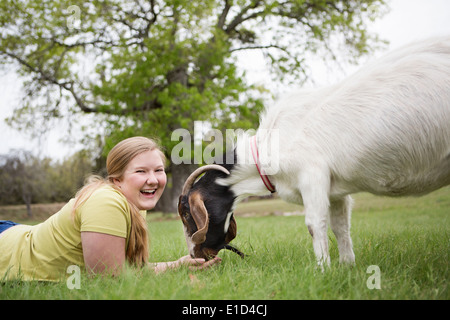 A girl lying on grass head to head with a goat. Stock Photo