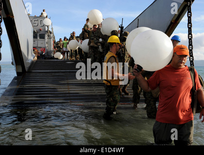 U.S. Navy Seabees, Marines and civilians from nongovernmental organizations carry water jugs off a landing craft utility (LCU) Stock Photo