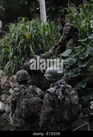 Afghan National Army (ANA) soldiers of the 201st ANA Corps help each other navigate an incline while patrolling farm fields en Stock Photo