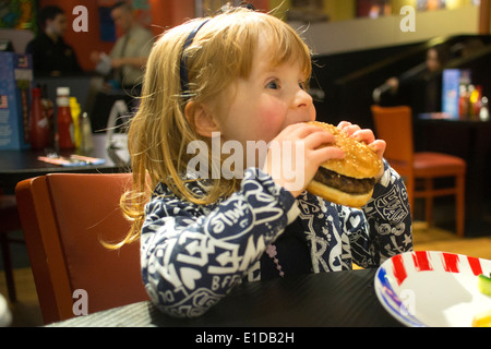 Four 4 year old girl in restaurant eating cheese burger Stock Photo