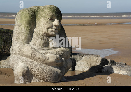 Blue sky view, across sandy beach to sea, stone Sea Ogre Sculpture standing end of boulder groyne, Cleveleys, Fylde Coast, UK Stock Photo