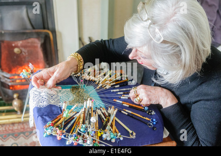 A woman hand-crafts intricate lace using old fashioned bobbins in her home. Stock Photo