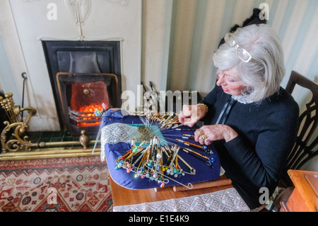 A woman hand-crafts intricate lace using old fashioned bobbins in her home. Stock Photo