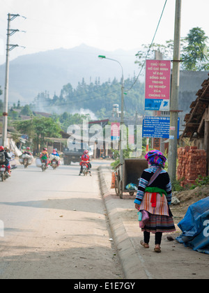 A street scene in Bac Ha, Lao Cai Province, Vietnam.  A Flower Hmong woman walks in the foreground. Stock Photo