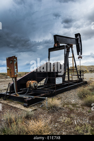 An idled oil pump-jack under dark stormy clouds. Wyoming, USA. Stock Photo