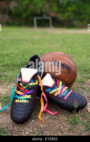 Good luck soccer football boots soccer cleats laced with Brazilian wish ribbons on rustic dirt grass pitch with vintage football Stock Photo