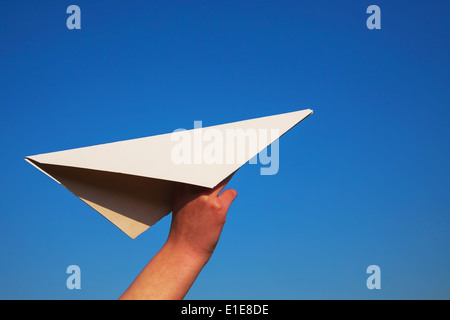 Hand holding paper plane against blue sky Stock Photo