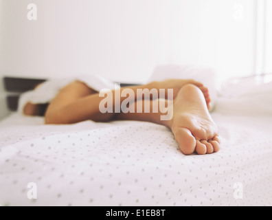 Feet of a woman sleeping in bed at home. Legs of a female lying on bed - Indoors Stock Photo