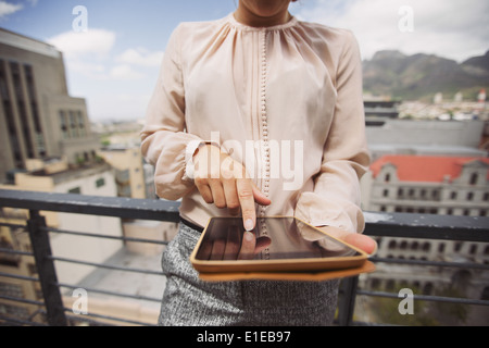 Cropped image of young woman working on tablet PC. Close up image of female standing on balcony using digital tablet. Stock Photo