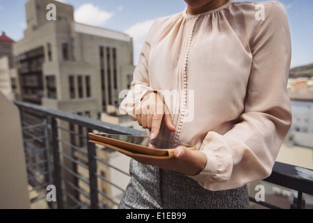 Young woman standing on balcony using tablet PC. Cropped image of female working on digital tablet. Stock Photo
